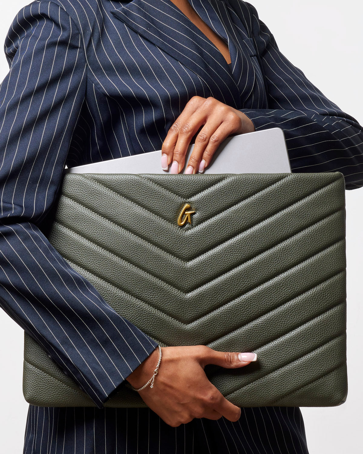 Olive green pebble laptop sleeve with chevron design, held by a woman in a pinstriped blazer.