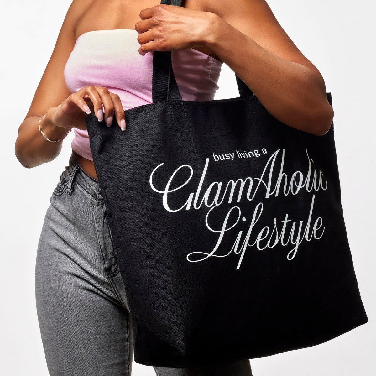 Black canvas tote bag featuring "busy living a Glam-Aholic Lifestyle" text, perfect for stylish everyday use.