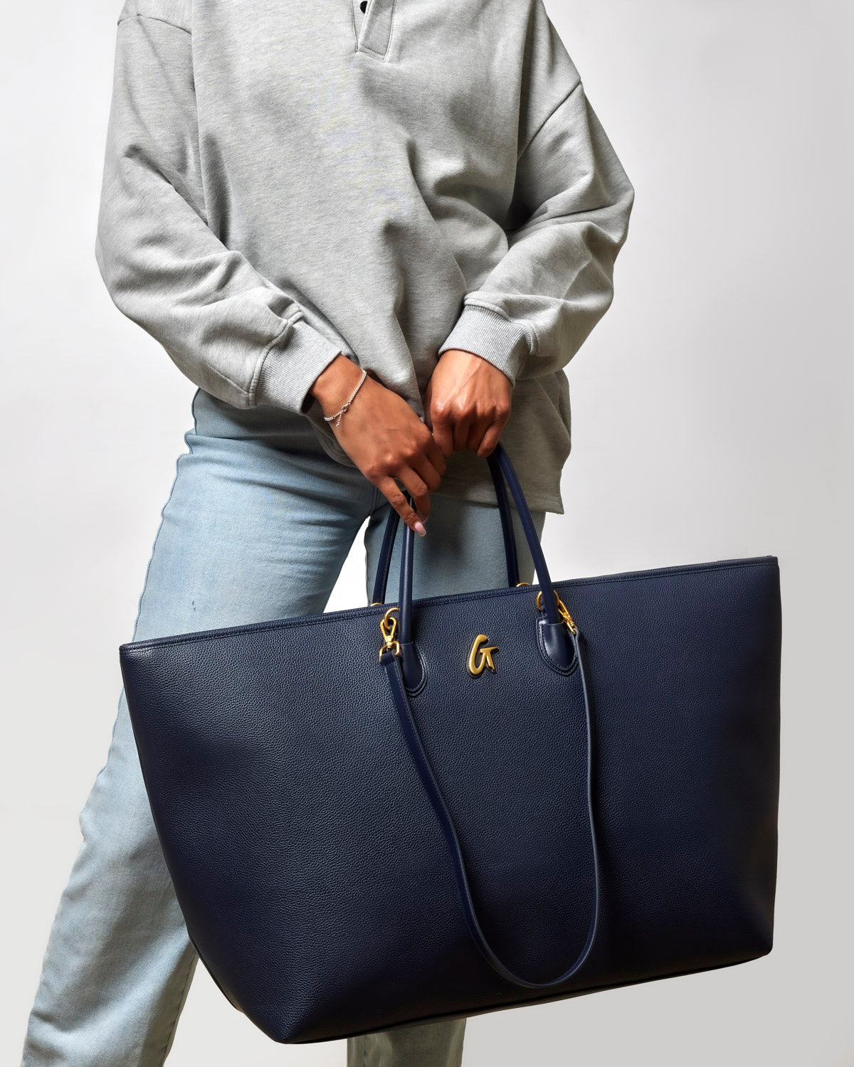 Navy jumbo pebble tote bag held by a person wearing a gray sweatshirt and light jeans, showcasing its spacious design.
