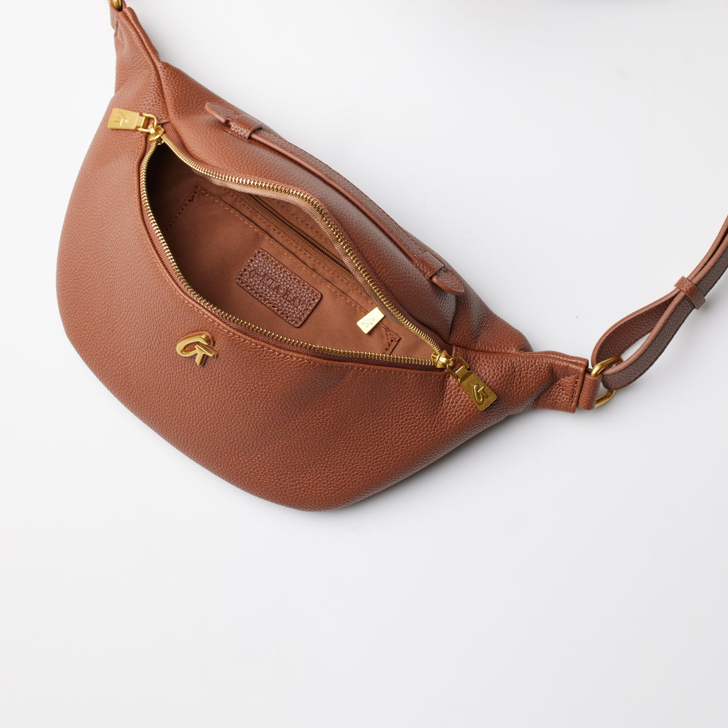Brown pebble-textured fanny pack with gold zipper and adjustable strap, shown open to reveal interior pocket and branding.