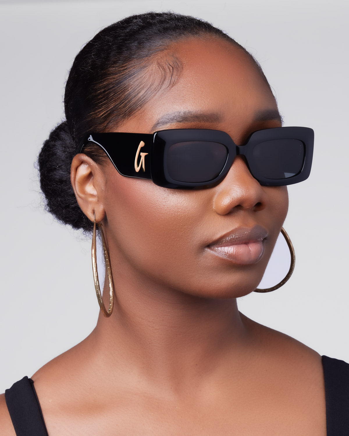 Stylish black sunglasses with a bold square frame, worn by a model with hoop earrings and a sleek hairstyle.