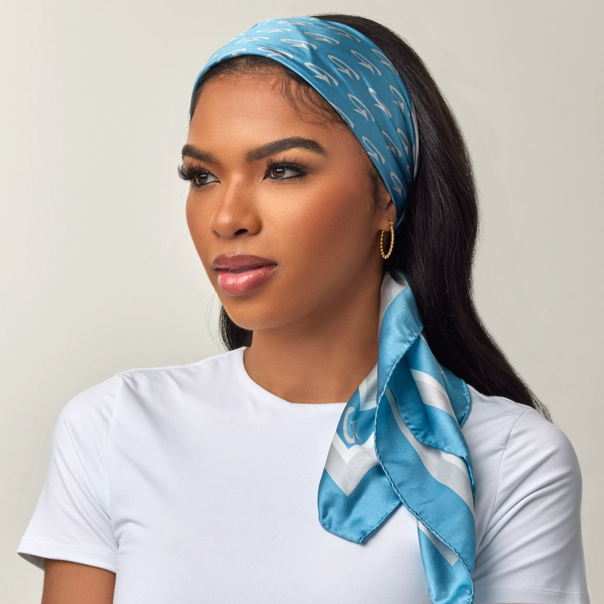 Woman wearing a blue patterned silk headscarf, gold hoop earrings, and a white top, showcasing affordable luxury accessories.