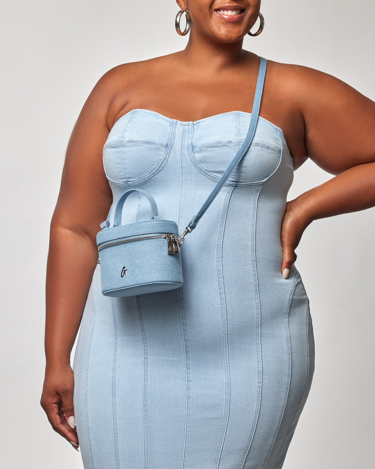 Mini denim silver vanity bag with a zipper closure, worn crossbody by a woman in a light denim dress.