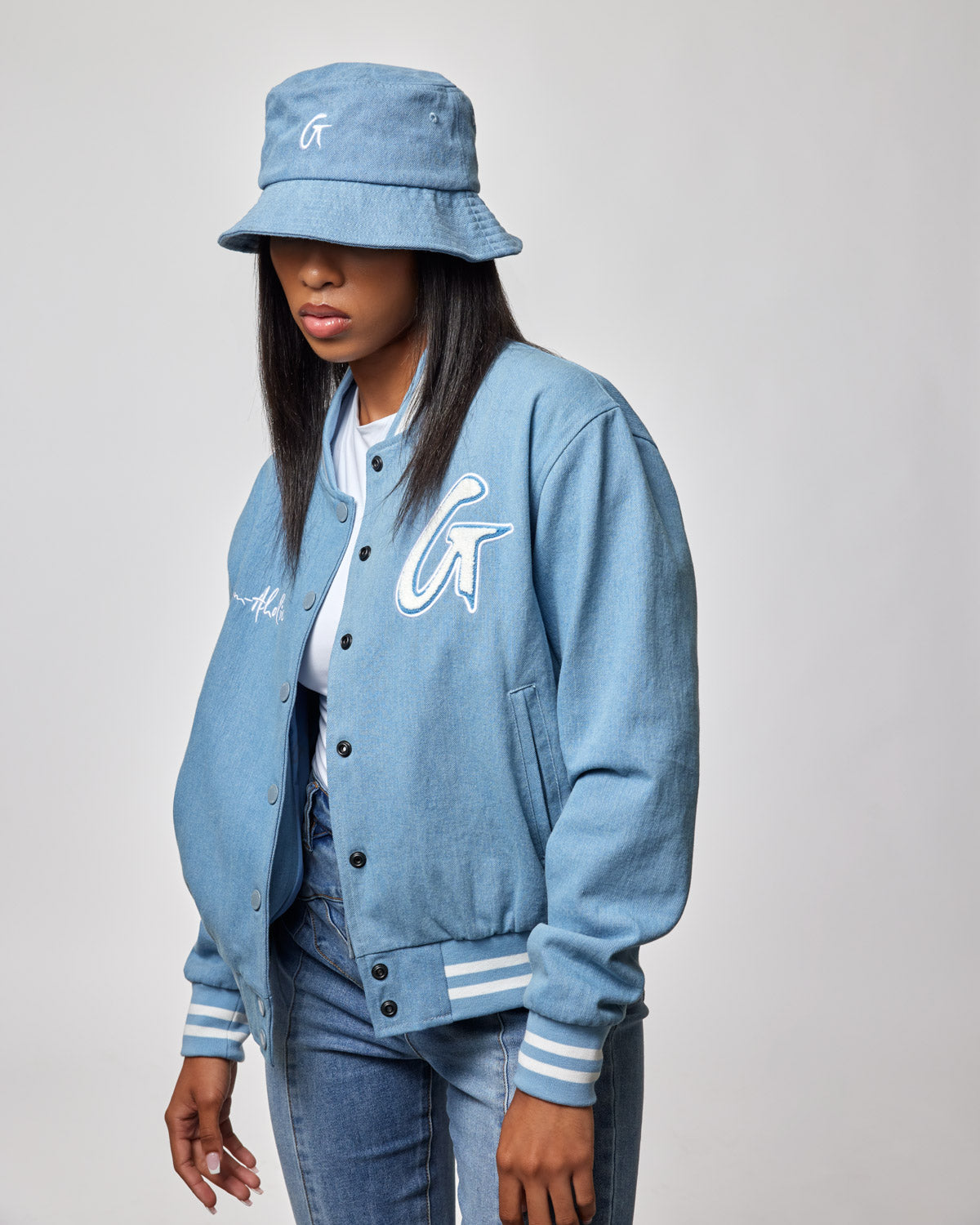 Woman wearing a light blue denim bucket hat, matching denim varsity jacket, and jeans, with a casual streetwear style.