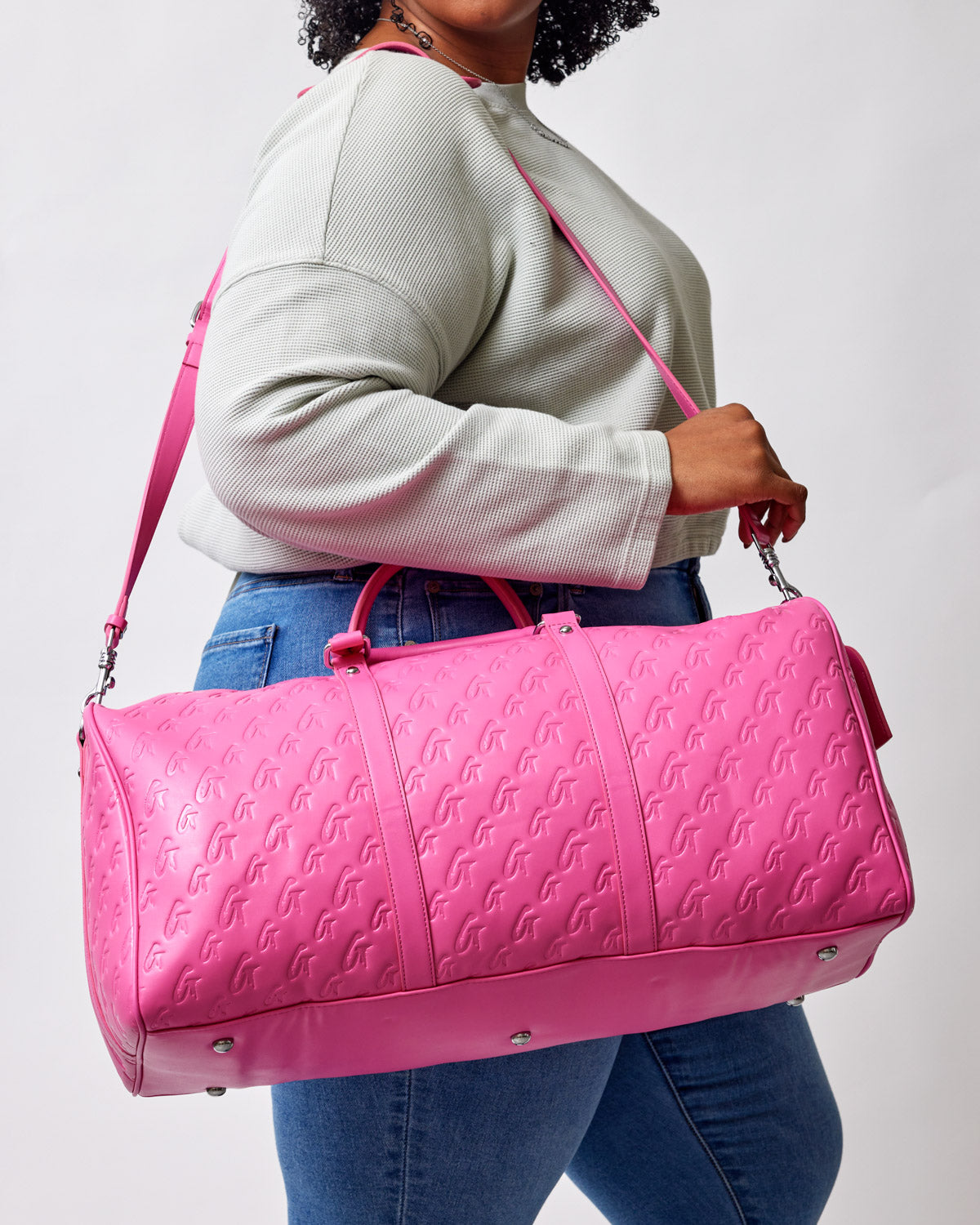 Hot pink monogram duffle bag with embossed logo pattern, carried by a woman in a casual outfit.