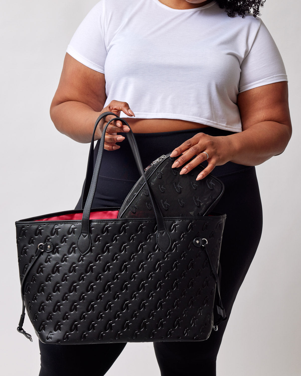 Black and pink monogram tote bag held by a woman, featuring a spacious interior and a matching pouch inside.