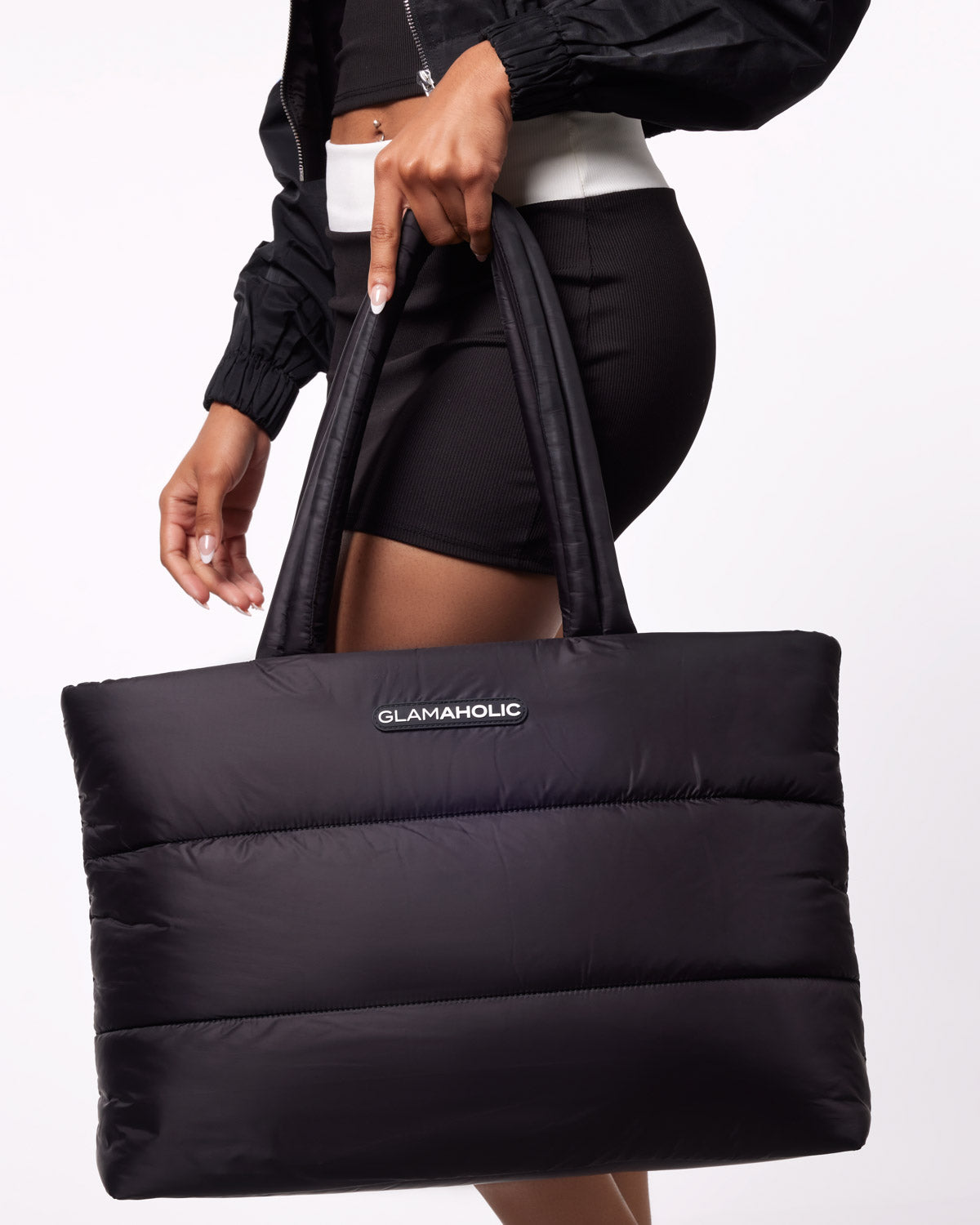 Black athletic nylon tote bag held by a model, featuring a padded design and the Glam-Aholic logo.