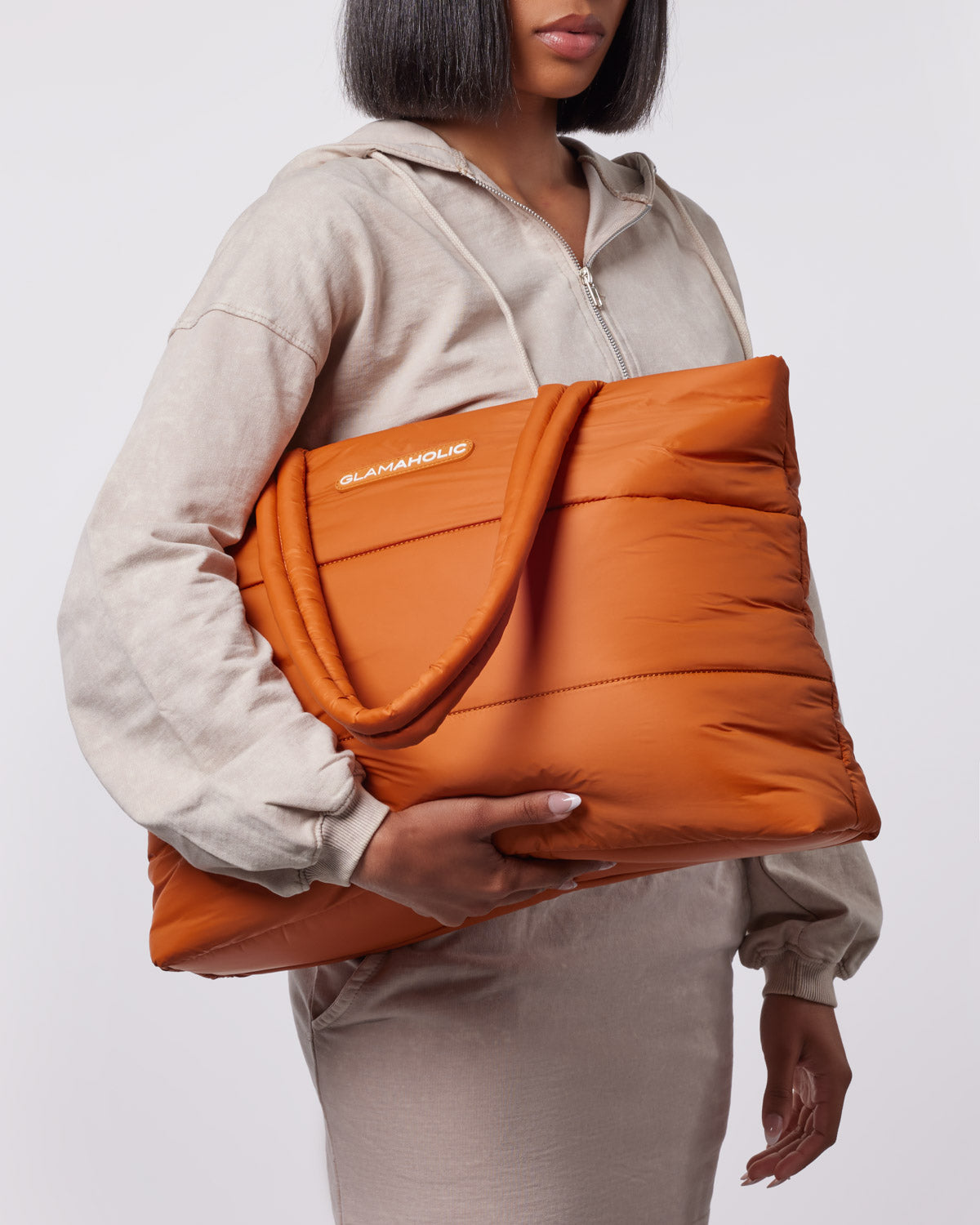 Brown athletic nylon tote bag held by a person in a light gray outfit, showcasing its stylish and functional design.