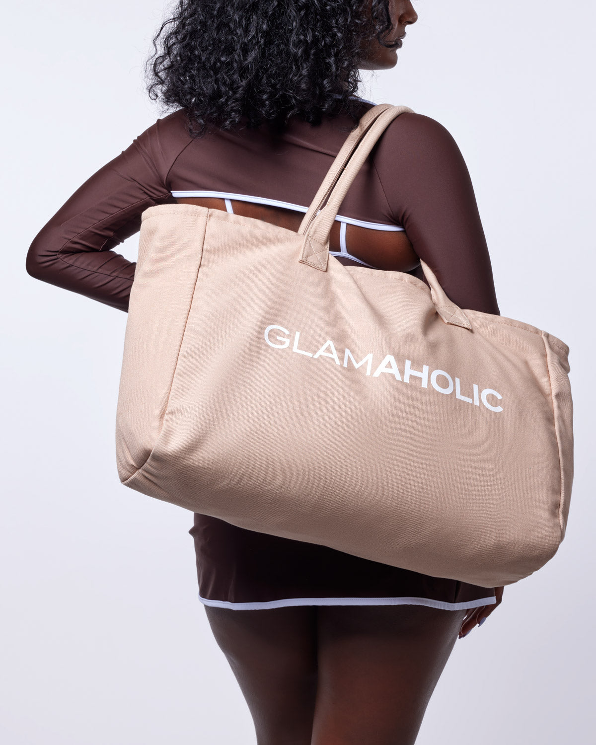 Nude athletic canvas tote bag featuring the Glam-Aholic logo, carried by a model against a neutral background.