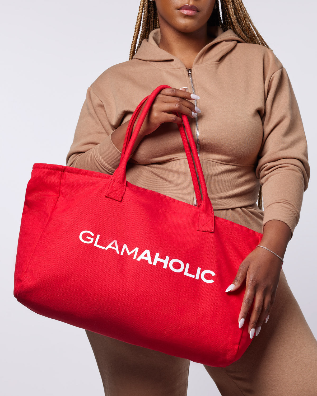 Red athletic canvas tote bag featuring the word "GLAMAHOLIC" prominently displayed, held by a model in a beige outfit.
