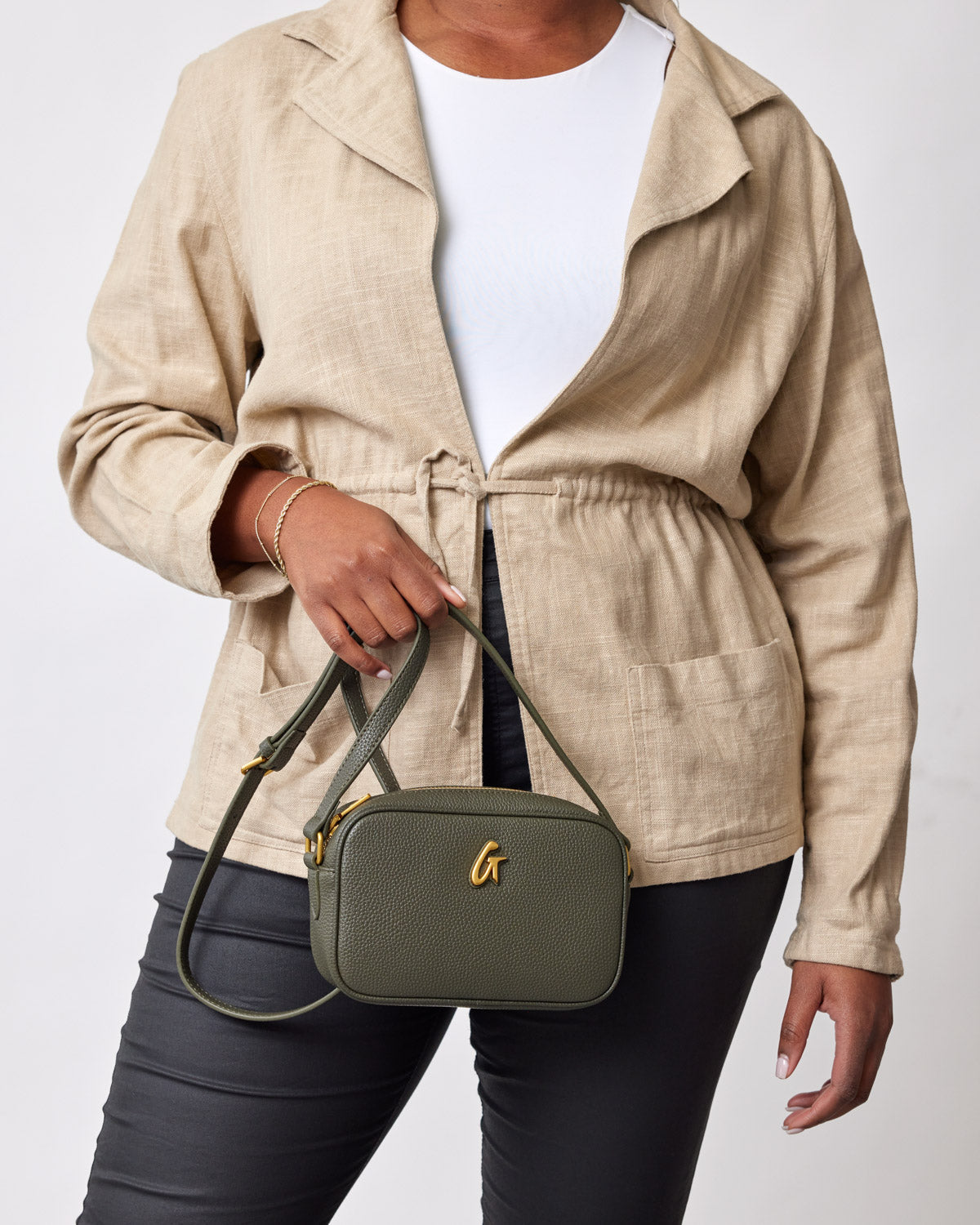 Mini Pebble Camera Bag in olive green, held by a woman wearing a beige jacket and black pants.