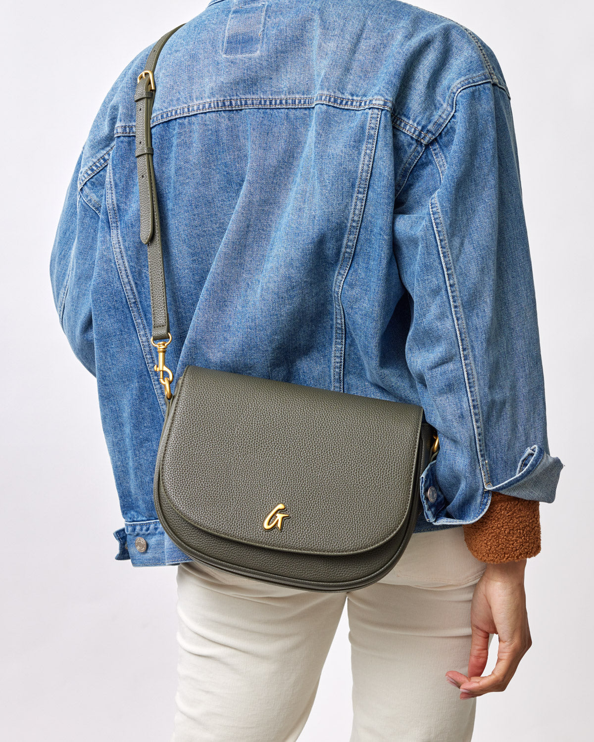 Large olive green pebble shoulder bag with a gold "G" logo, worn crossbody over a denim jacket.
