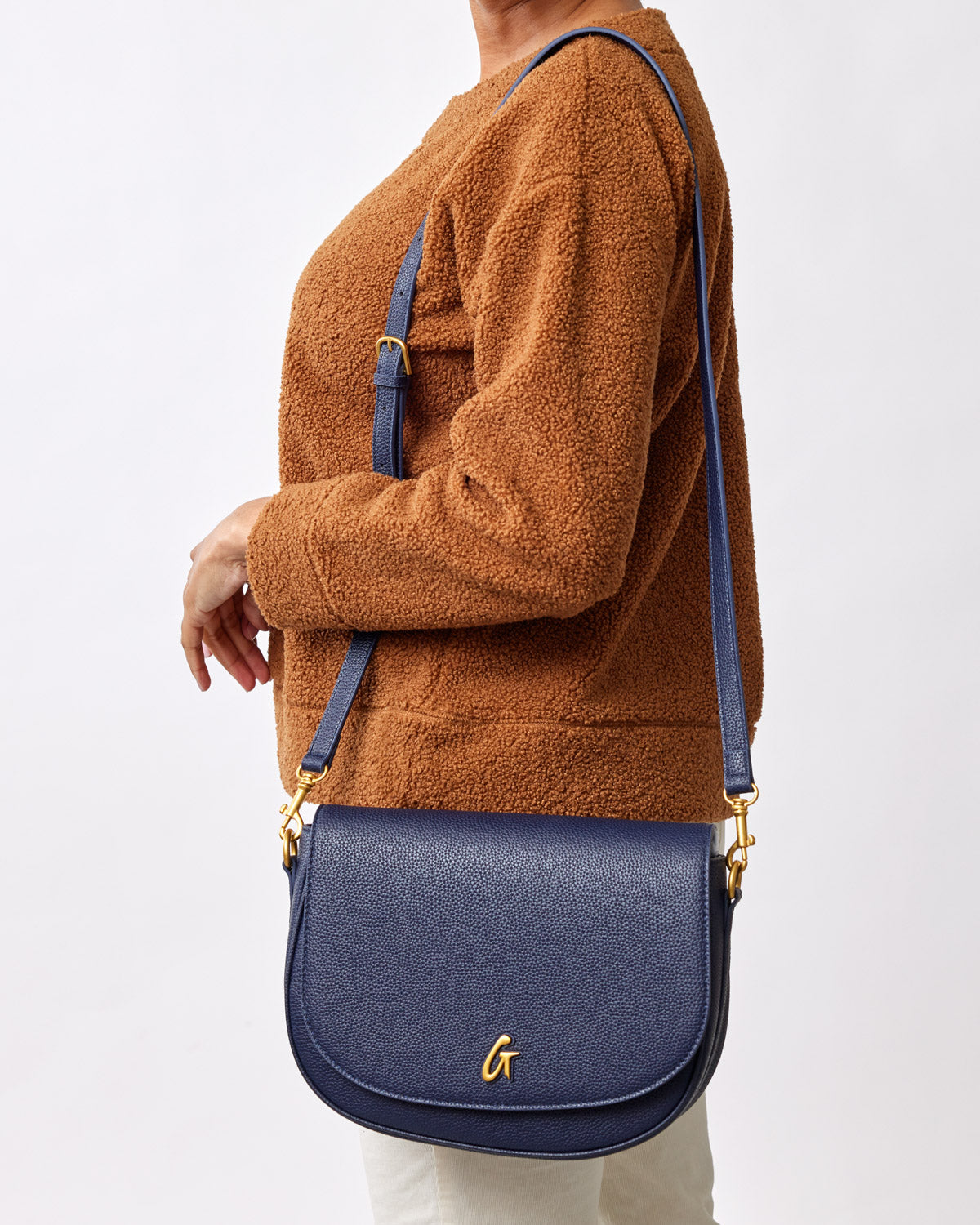 Large navy pebble shoulder bag with gold hardware, worn crossbody by a person in a brown fleece jacket.