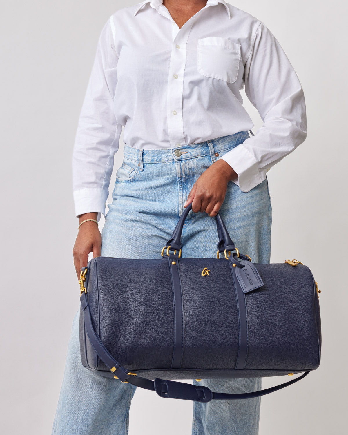 Navy Pebble Duffle Bag with gold hardware, held by a person wearing a white shirt and light blue jeans.