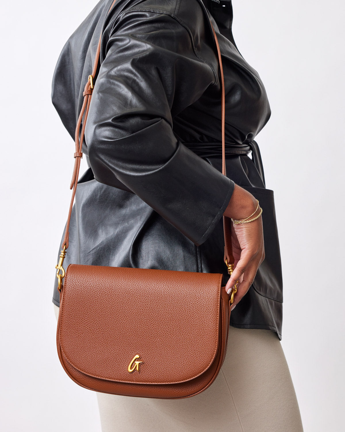 Brown textured leather handbag with a gold "G" logo, gold hardware, and a matching adjustable strap, styled with black lea...