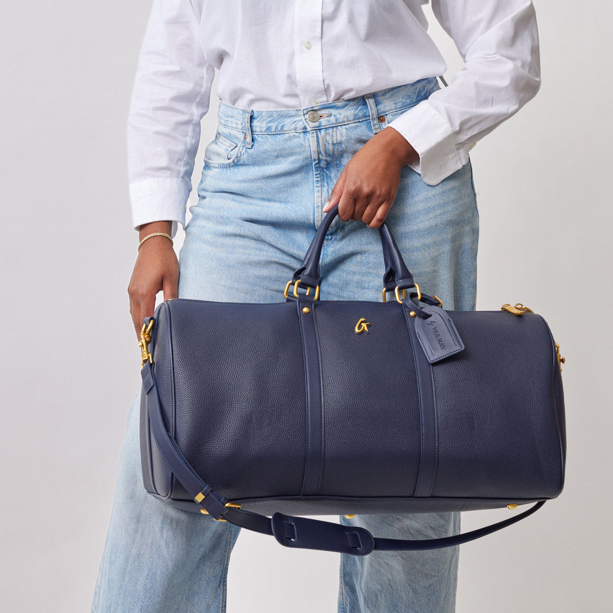 Navy blue textured leather duffle bag with gold hardware, top handles, adjustable shoulder strap, and designer logo charm.