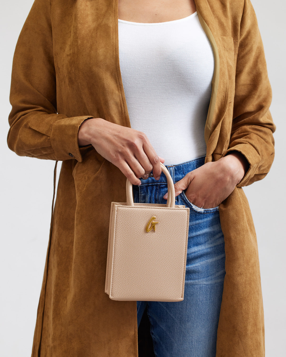 Mini Pebble Tote in nude color, held by a woman wearing a white top, blue jeans, and a brown coat.