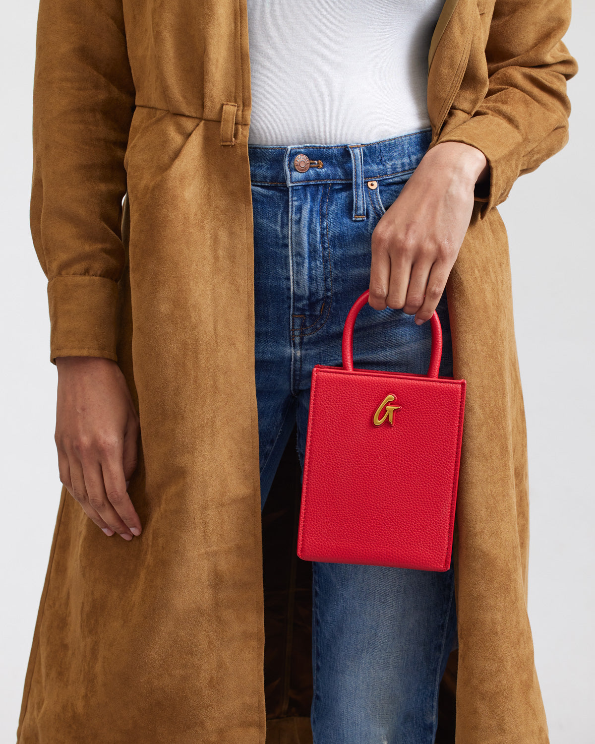Red mini pebble tote bag with a gold "G" logo, held by a person wearing blue jeans and a tan coat.