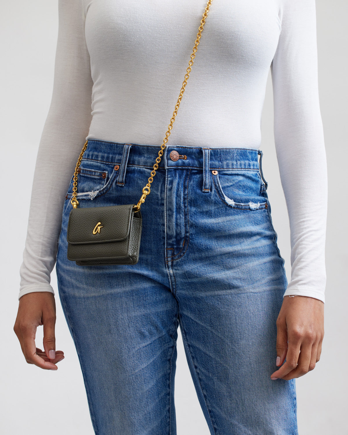 Mini Pebble WOC in olive green with a gold chain strap and gold logo, worn crossbody over casual blue jeans and white top.