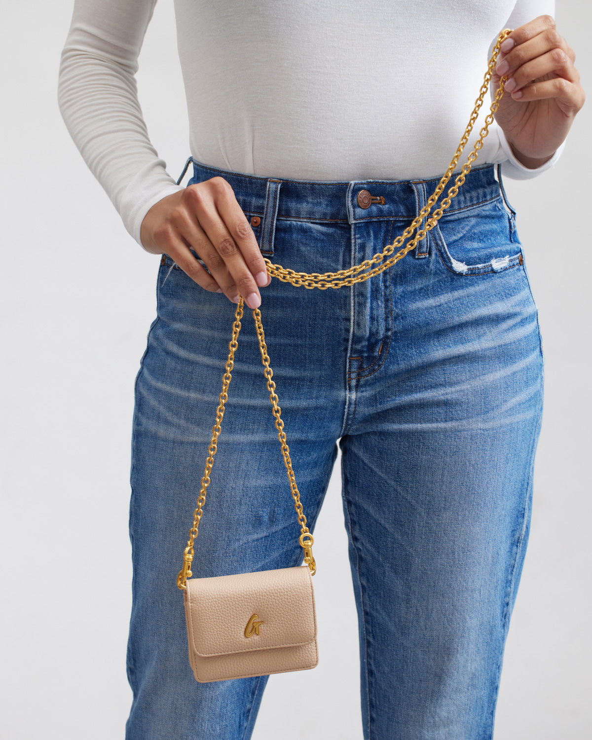 Mini Pebble WOC in nude color with gold chain strap, held by a person wearing blue jeans and a white top.