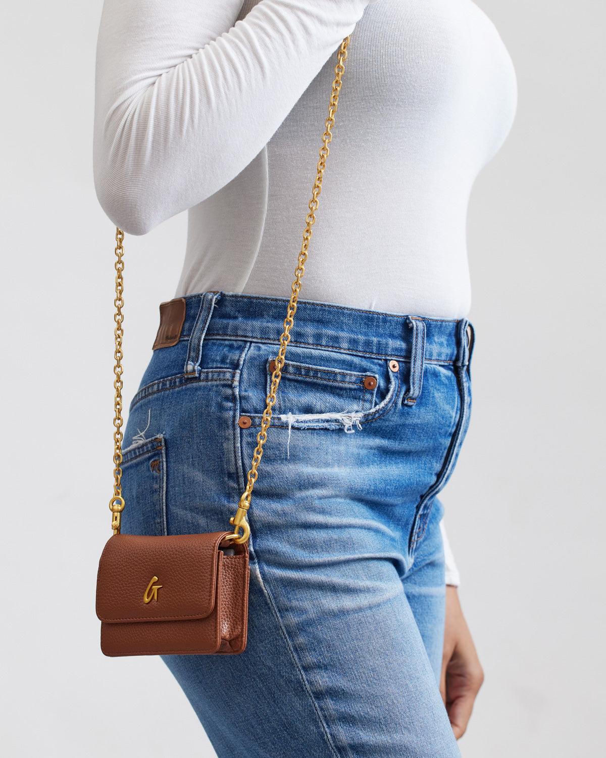 Mini Pebble WOC in brown with a gold chain, worn crossbody over casual blue jeans and a white long-sleeve top.