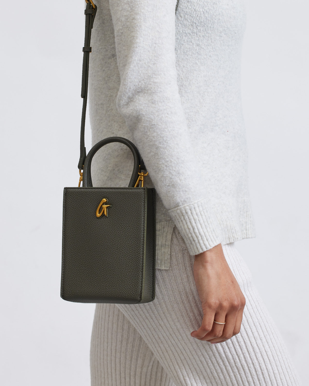 Mini Pebble Tote in olive green with gold logo, featuring textured leather, held by a person in cozy knitwear.