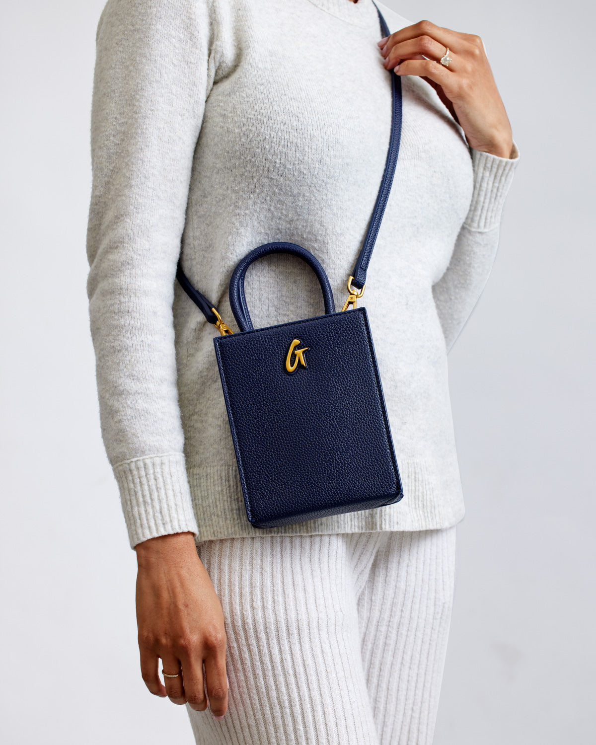 Mini Pebble Tote in navy with gold hardware, featuring a textured leather finish and a top handle, worn crossbody style.