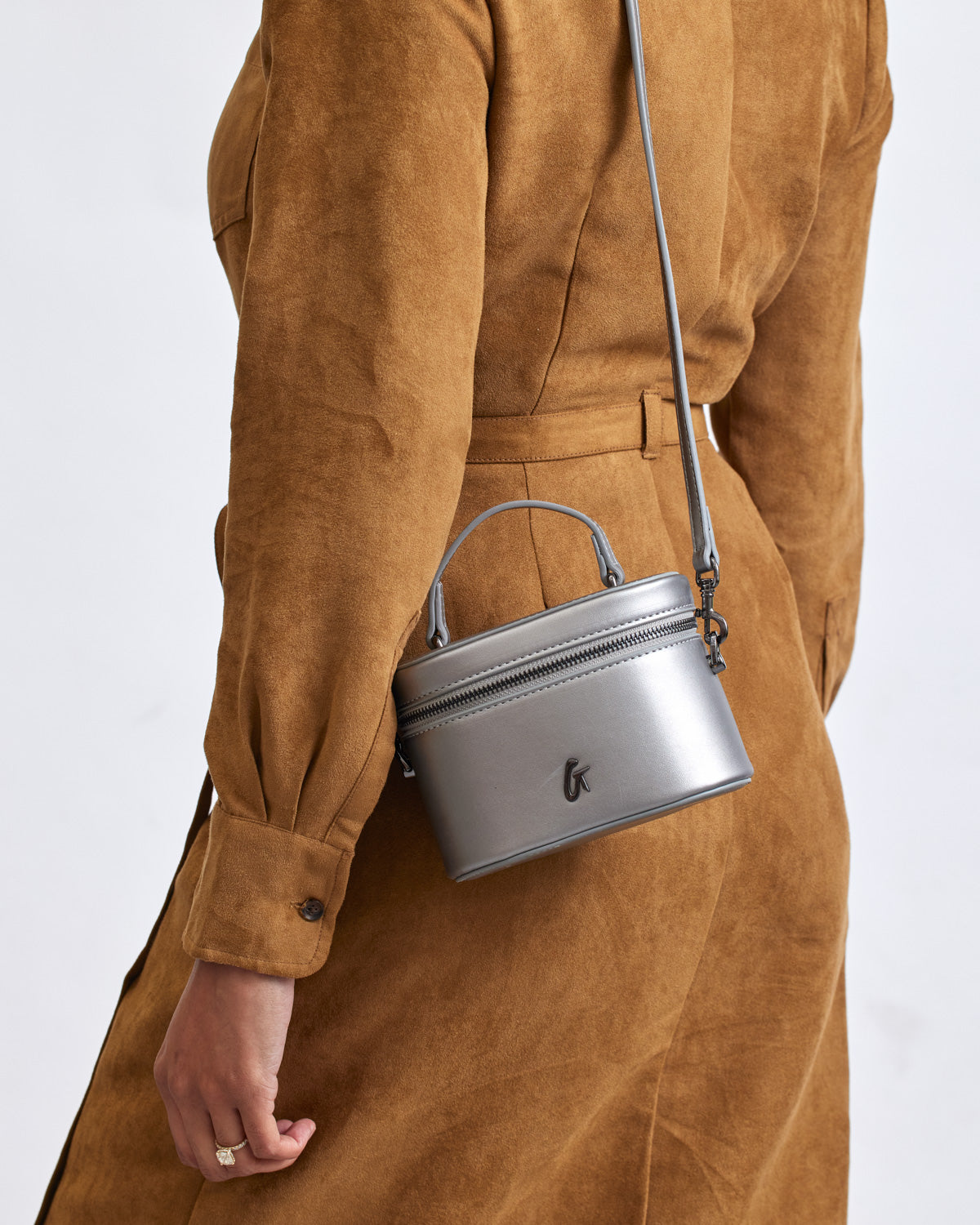 Mini smooth gunmetal vanity bag in platinum with a sleek, compact design, hanging from a person's shoulder against a brown outfit.