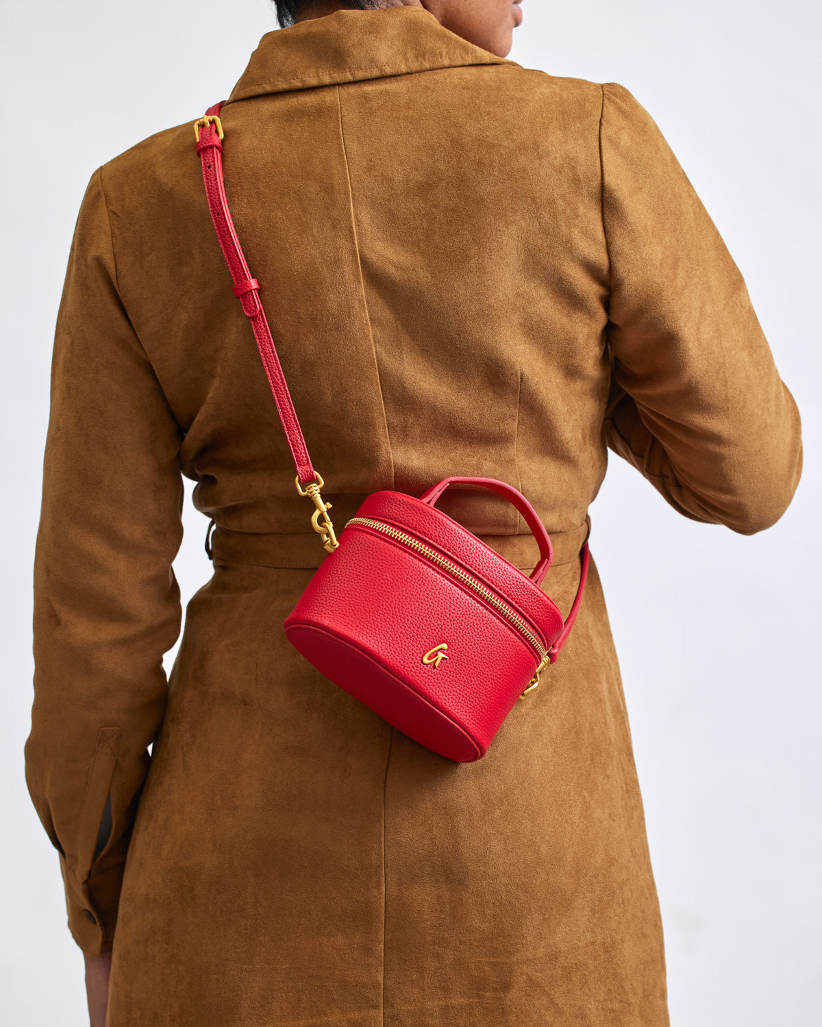 Red mini pebble vanity bag with gold zipper and logo, worn crossbody over a brown coat.