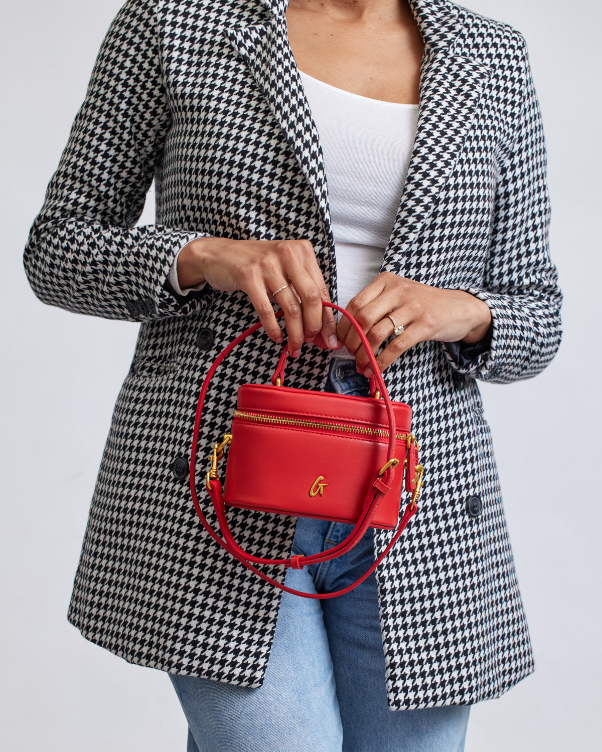 Mini smooth red vanity bag with gold accents, held by a woman in a black-and-white houndstooth blazer.