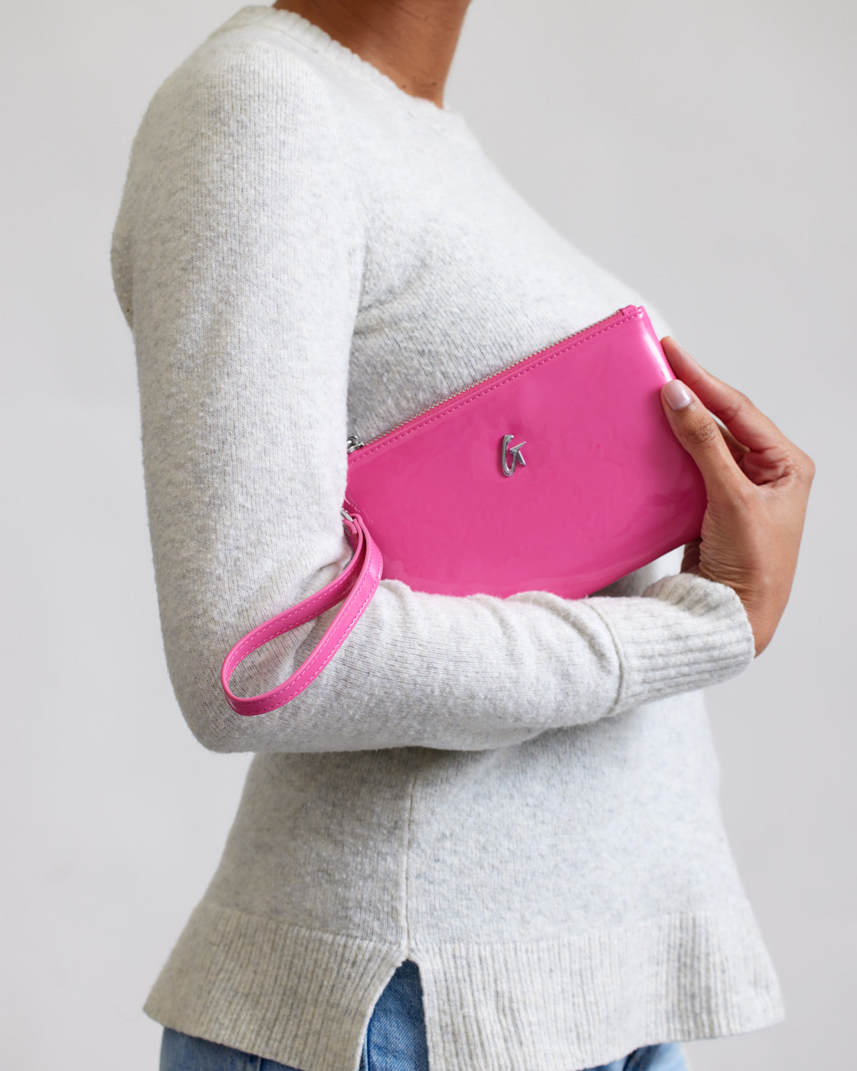 Mini silver wristlet with mirror finish in hot pink, featuring a wrist strap and a small logo on the front.