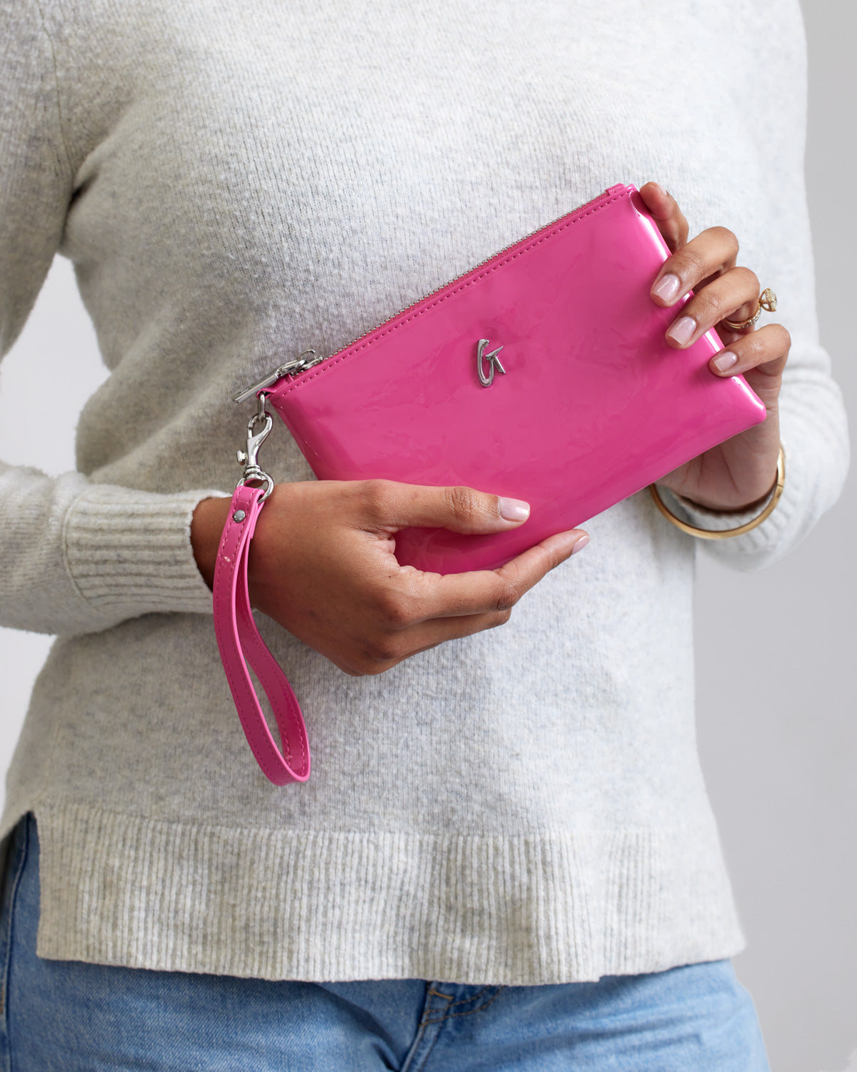 Mini silver wristlet with mirror finish in hot pink, featuring a wrist strap and a silver logo on the front.