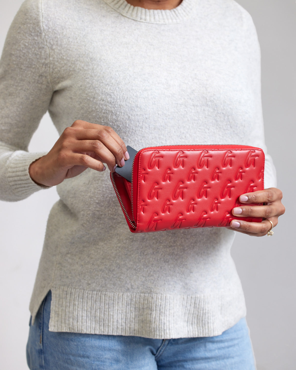 Red jumbo monogram wallet with embossed G logo pattern, being held by a woman in a light sweater.