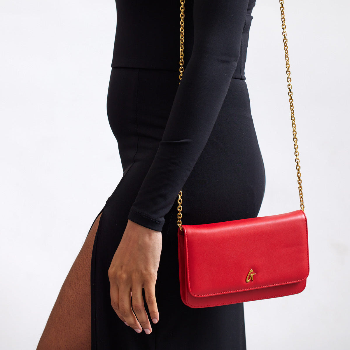 Red STANDARD GOLD WOC handbag with a gold chain strap, styled elegantly against a black outfit.