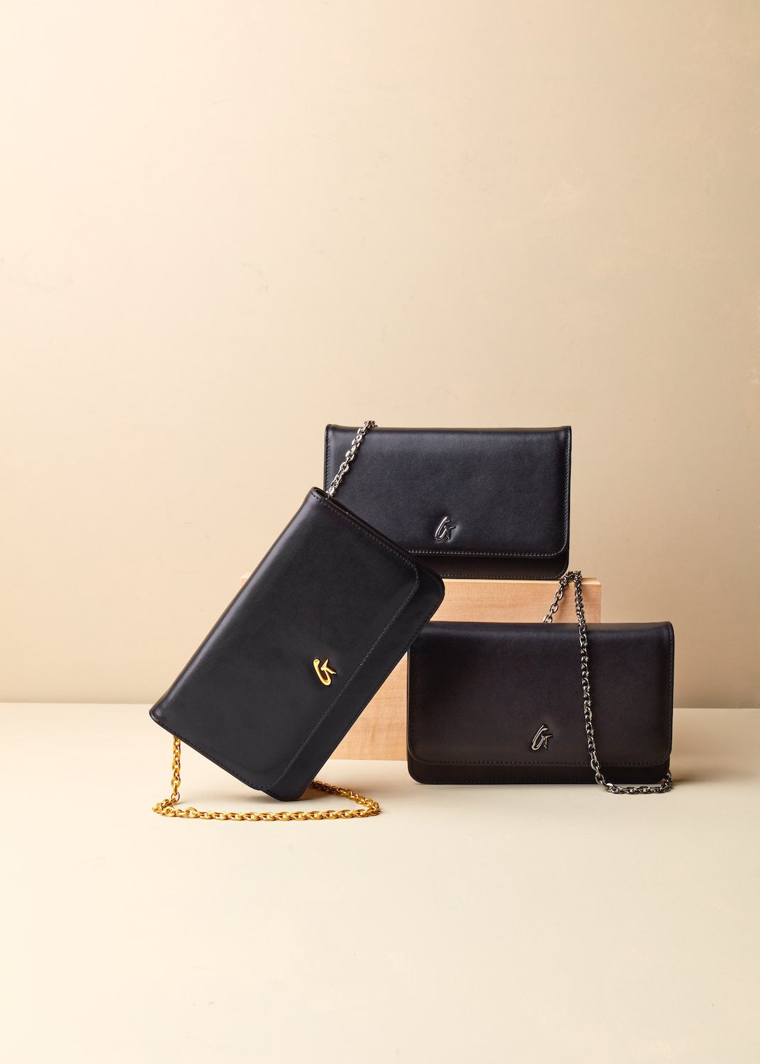 Black leather wallets with chain straps, featuring gold and silver logo accents, arranged on a beige surface.