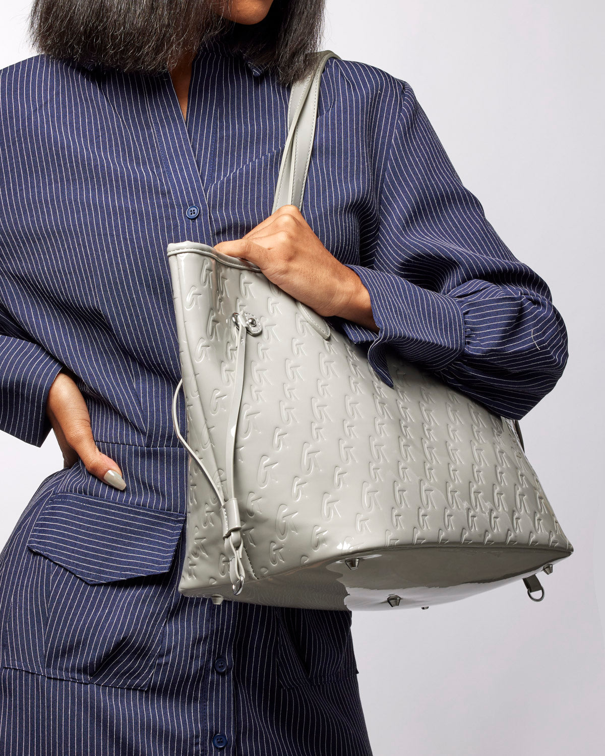 Stylish woman holding a mirror gray monogram tote bag, showcasing its sleek design and luxury appeal.