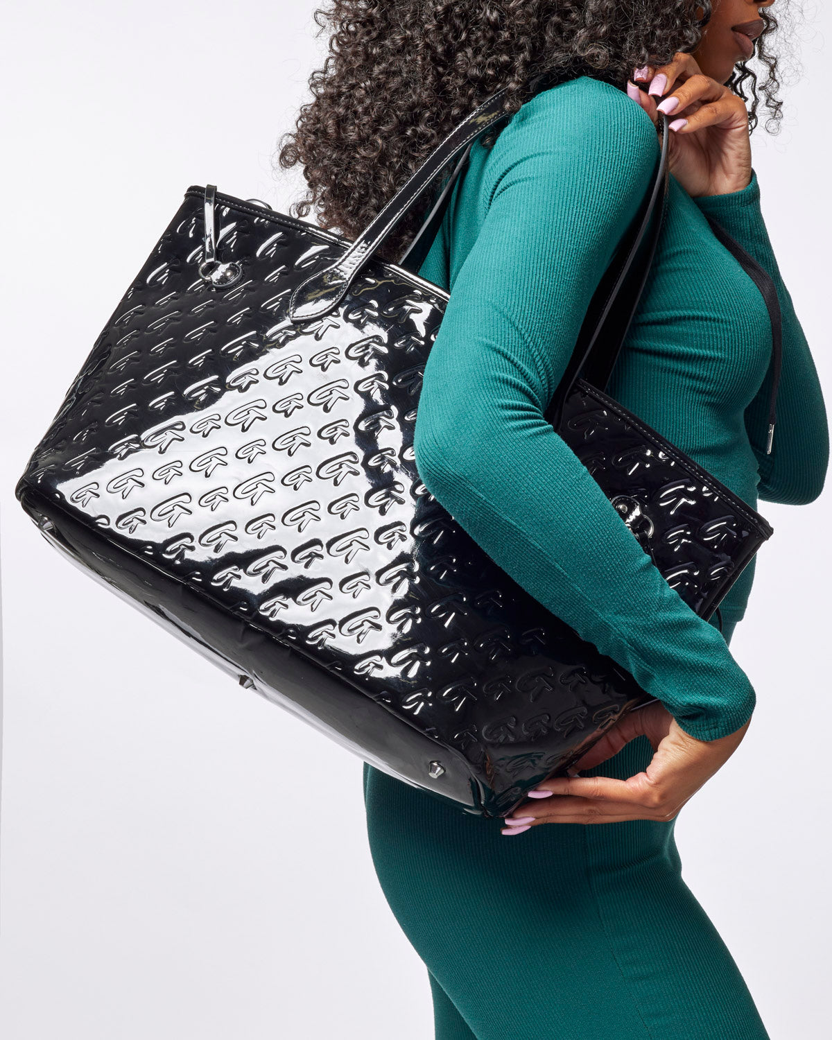 Stylish woman carrying the Monogram Glam Tote in mirror black, showcasing its glossy finish and spacious design.