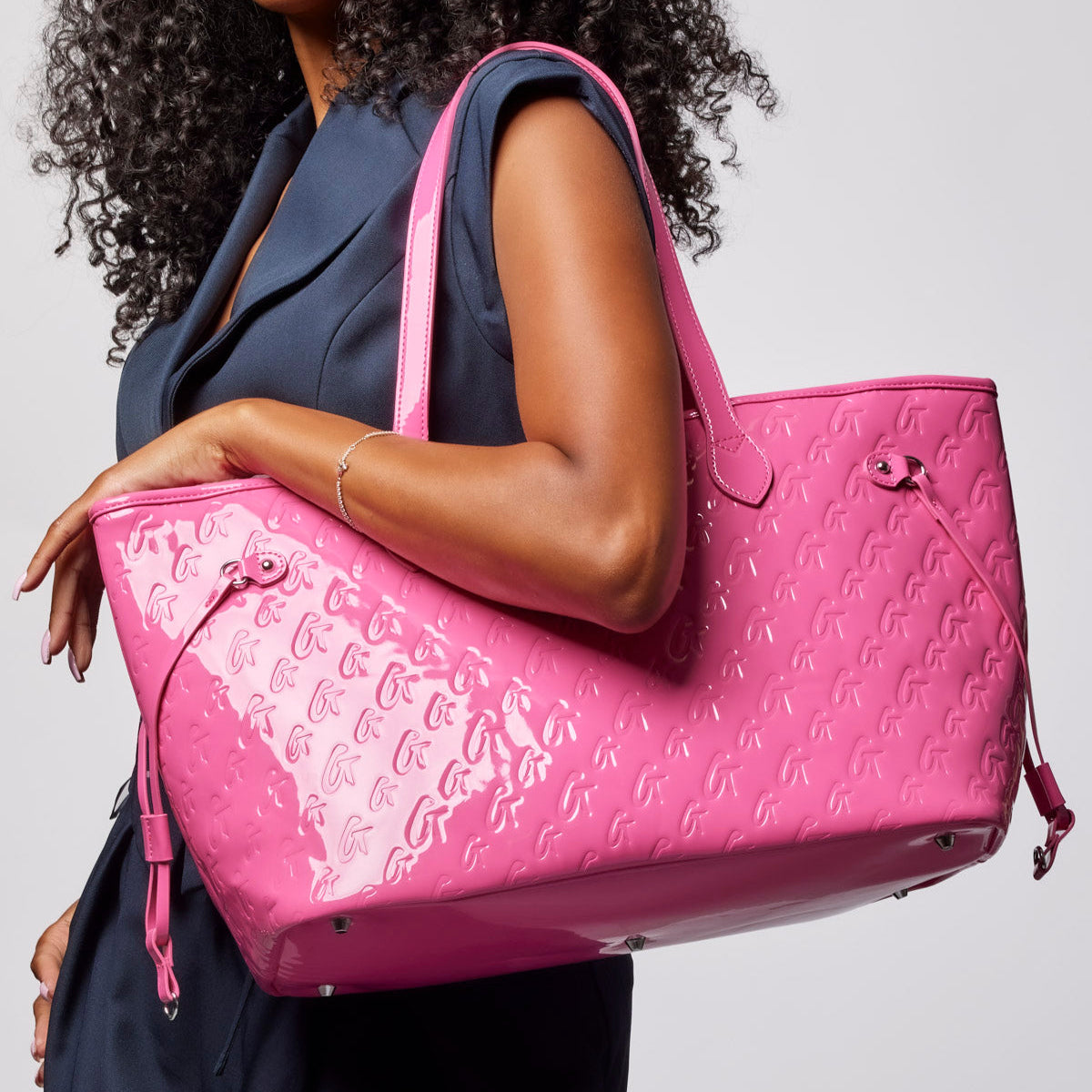 Hot pink monogram tote bag held by a model, featuring a glossy finish and spacious design for stylish everyday use.