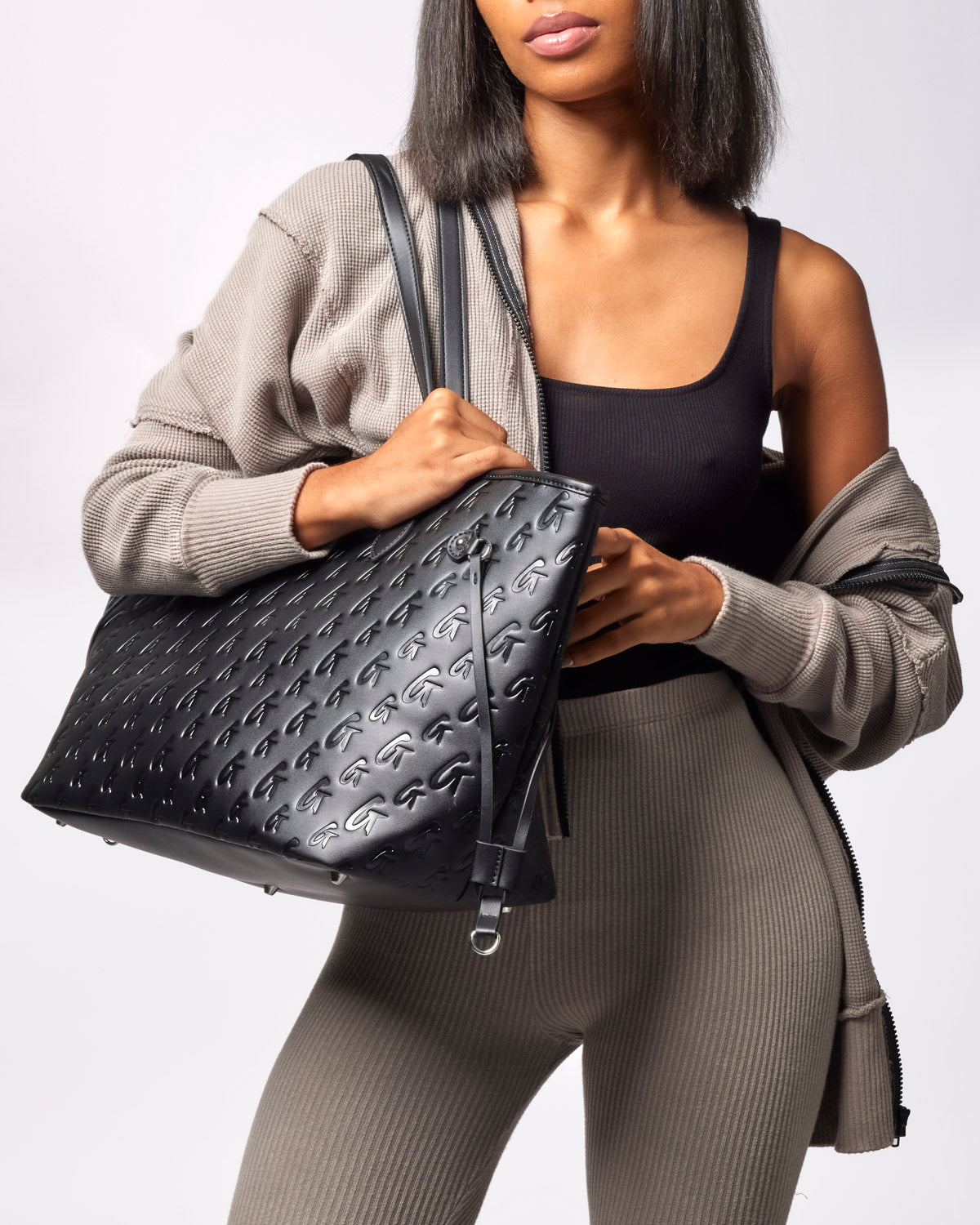 Stylish black monogram tote bag held by a woman, featuring a textured design and spacious interior for everyday use.