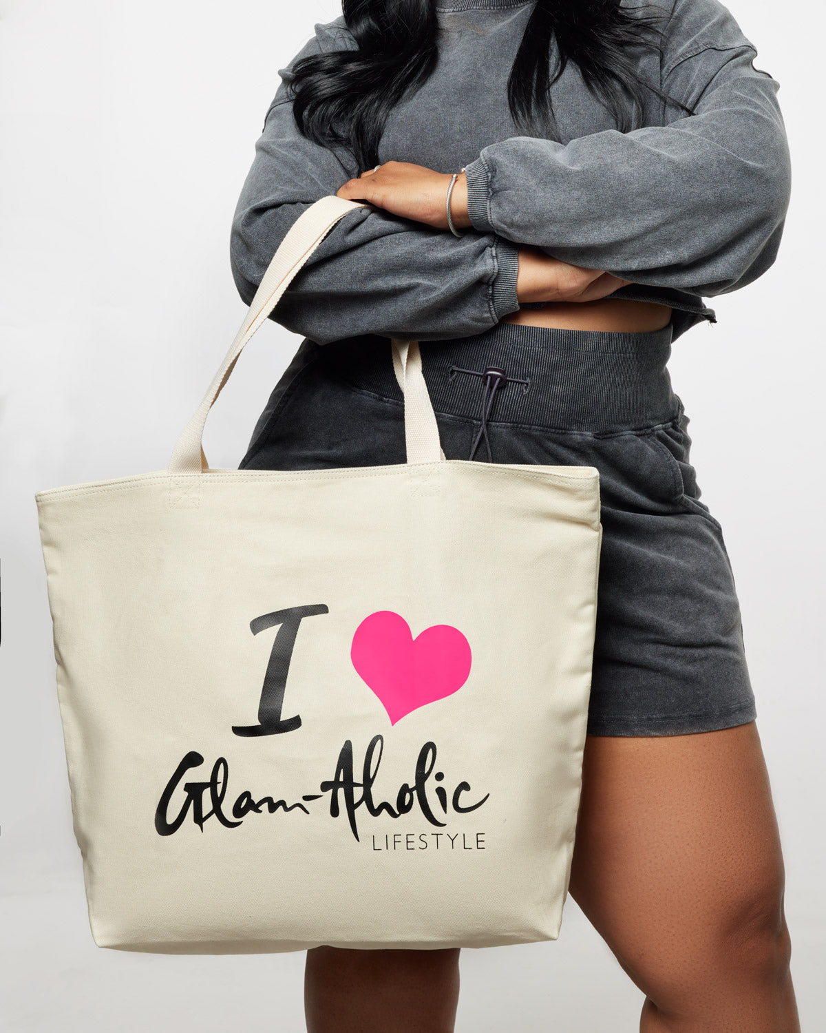 A woman holds a hot pink signature logo canvas tote bag with "I ♥ Glam-aholic Lifestyle" printed on it.