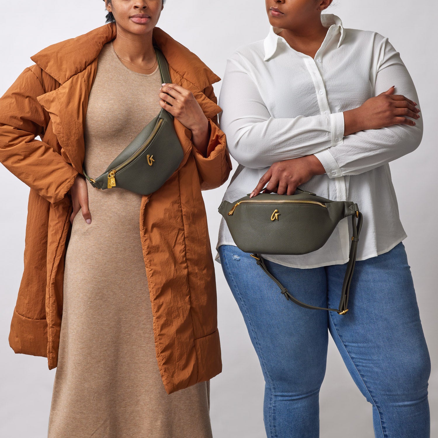 Two women hold olive green mini pebble fanny packs with gold zippers and logo, styled with casual outfits against a plain background.