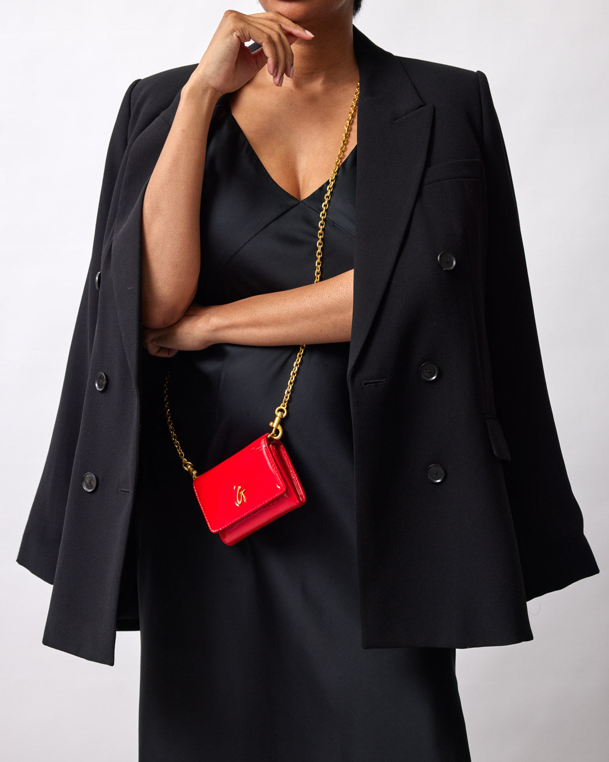 Red compact mirror with gold chain and logo, worn as a crossbody accessory over a black outfit and blazer.