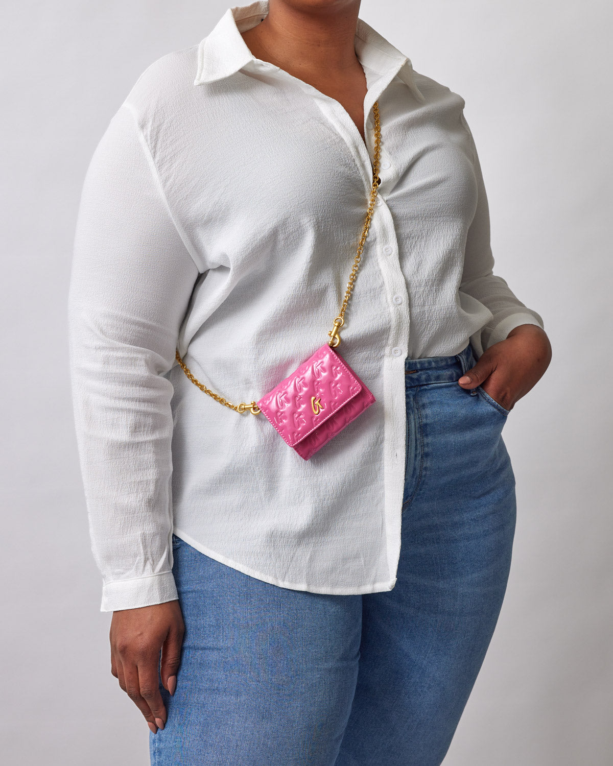 A woman wearing a white shirt and blue jeans, carrying a pink Monogram Gold Compact WOC mirror with a gold chain.