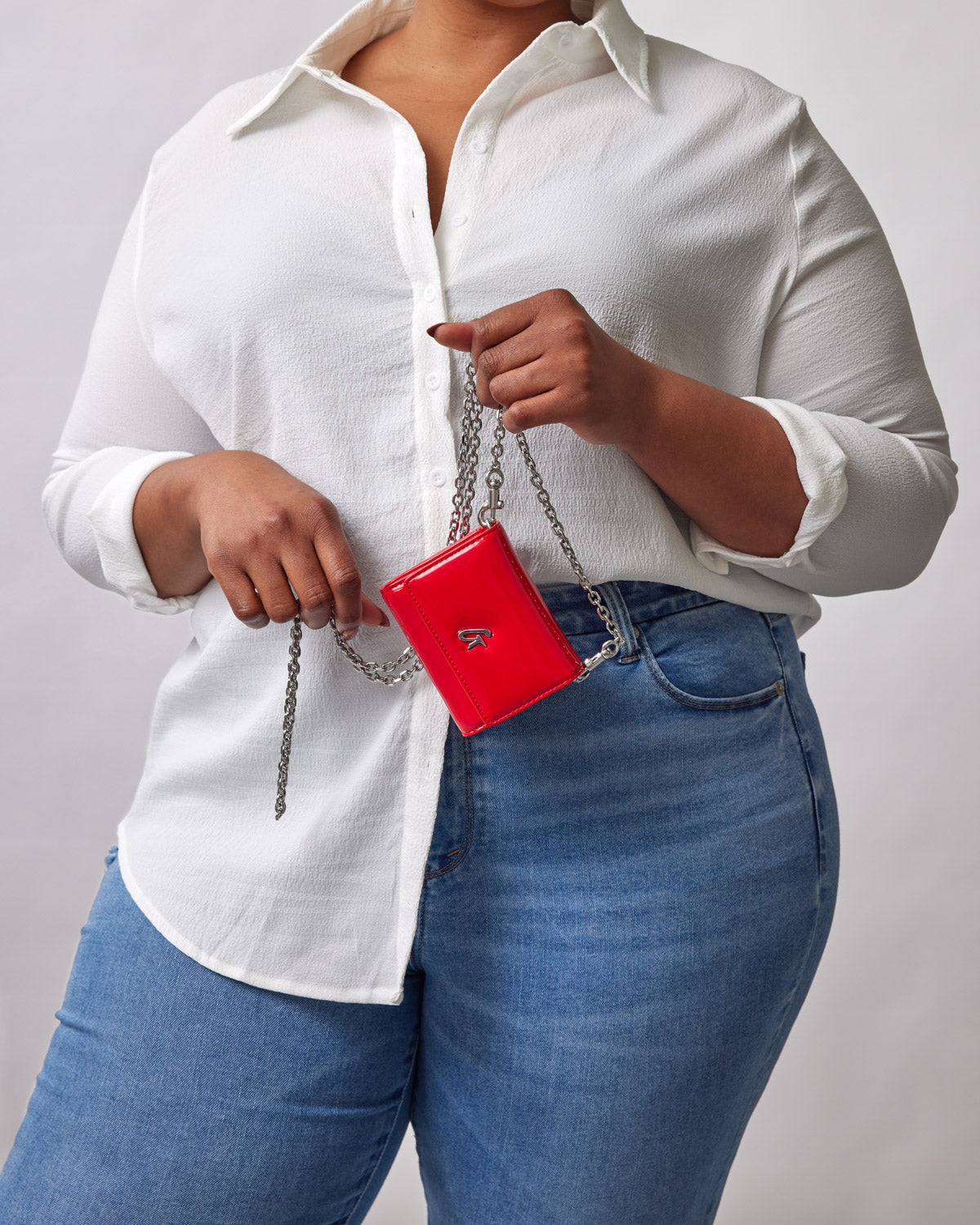 Red compact wallet with a silver chain and mirror, held by a woman wearing a white shirt and blue jeans.