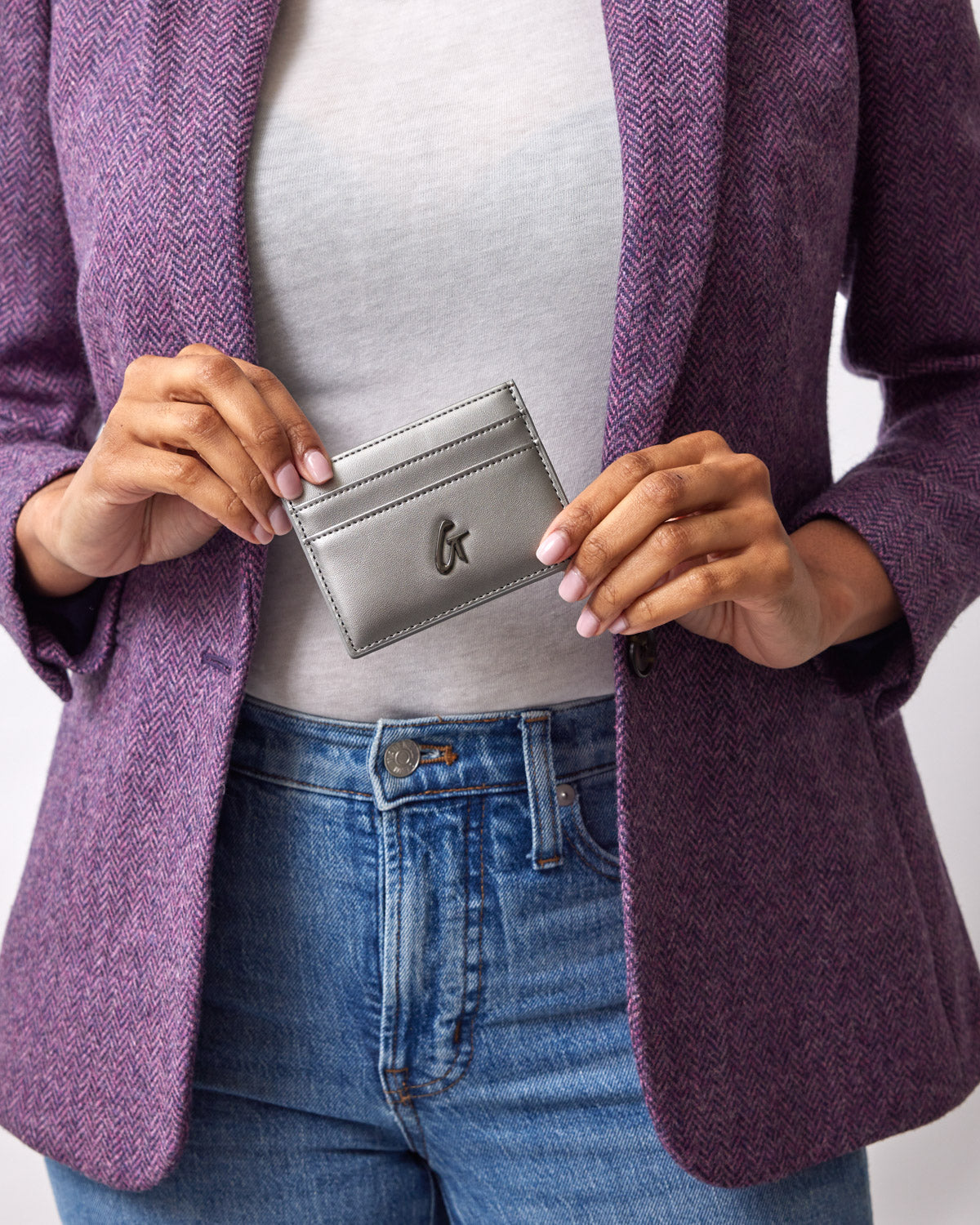 A person holding a silver gunmetal card holder with a logo, wearing a purple blazer, white top, and blue jeans.