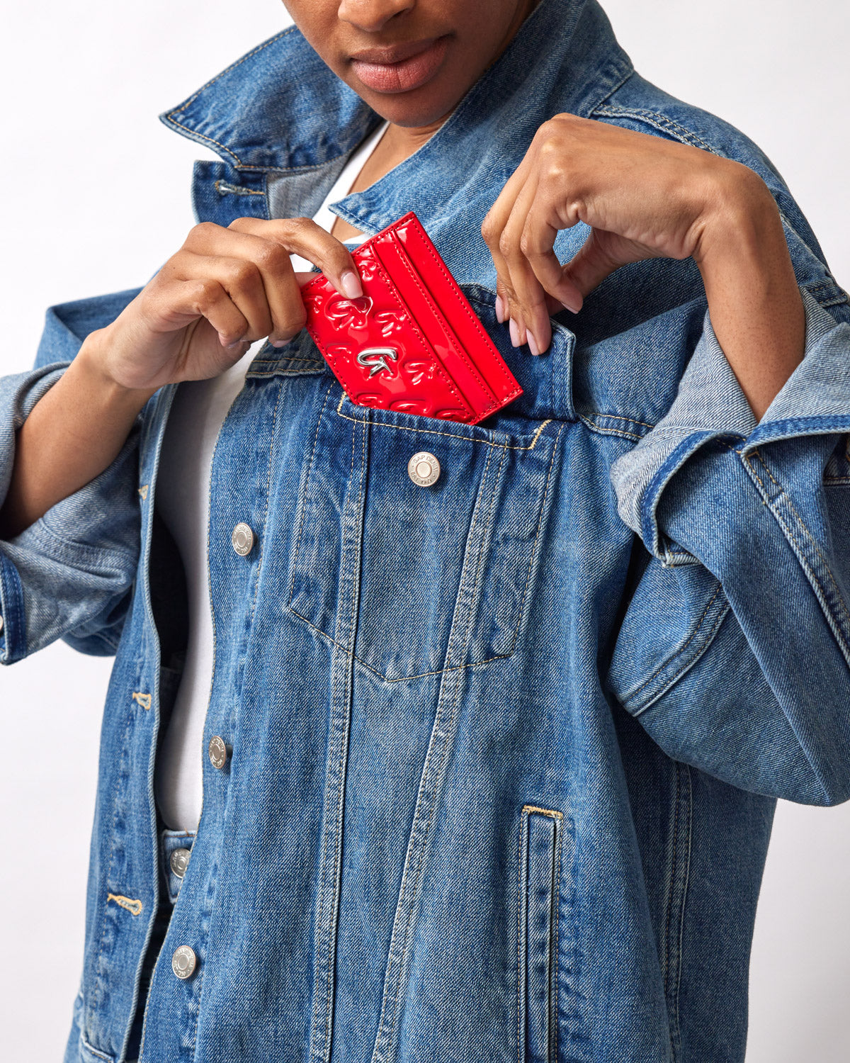 Woman in denim jacket placing a red mirror finish monogram silver card holder in her chest pocket.