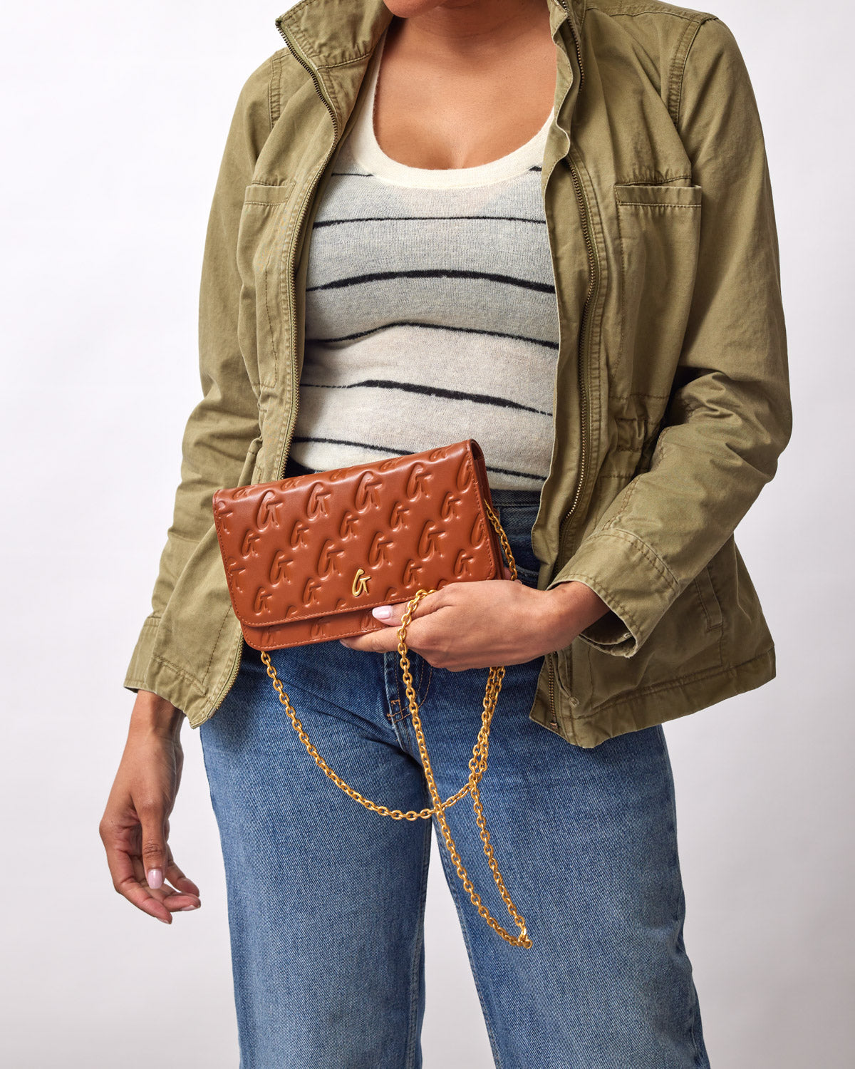 Brown Monogram Gold WOC handbag with embossed logo pattern and a gold chain strap, held by a woman in casual attire.