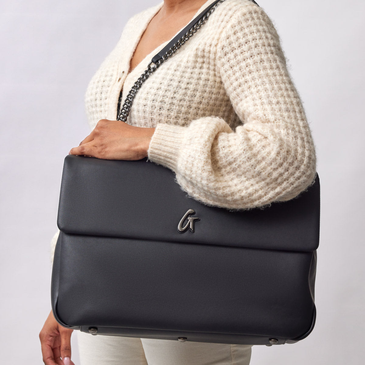 Black XL Standard Flap Bag with a chain strap, held by a woman in a cream sweater and beige pants.
