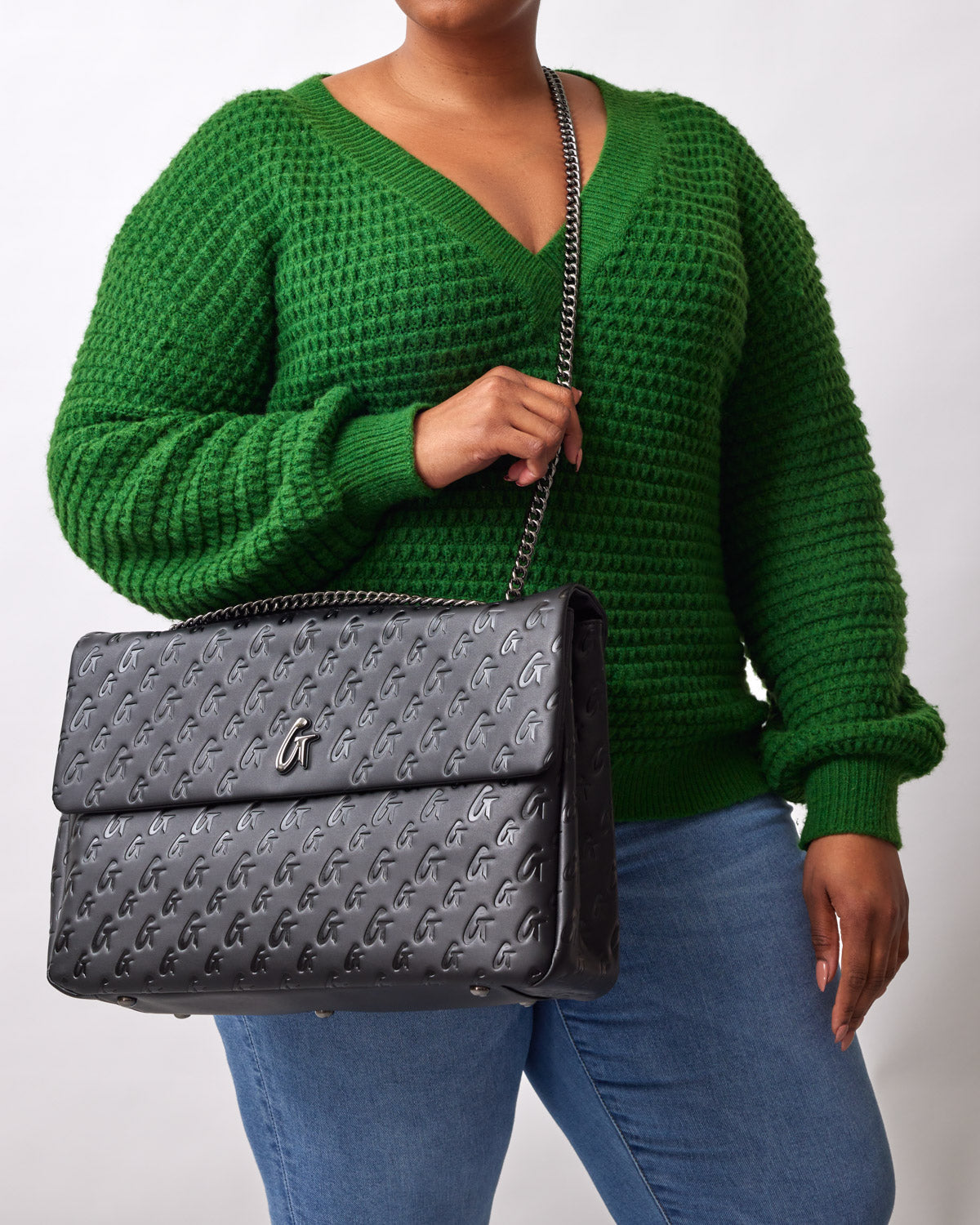 Black XL Monogram Flap Bag with embossed logo pattern, carried by a person in a green sweater and blue jeans.
