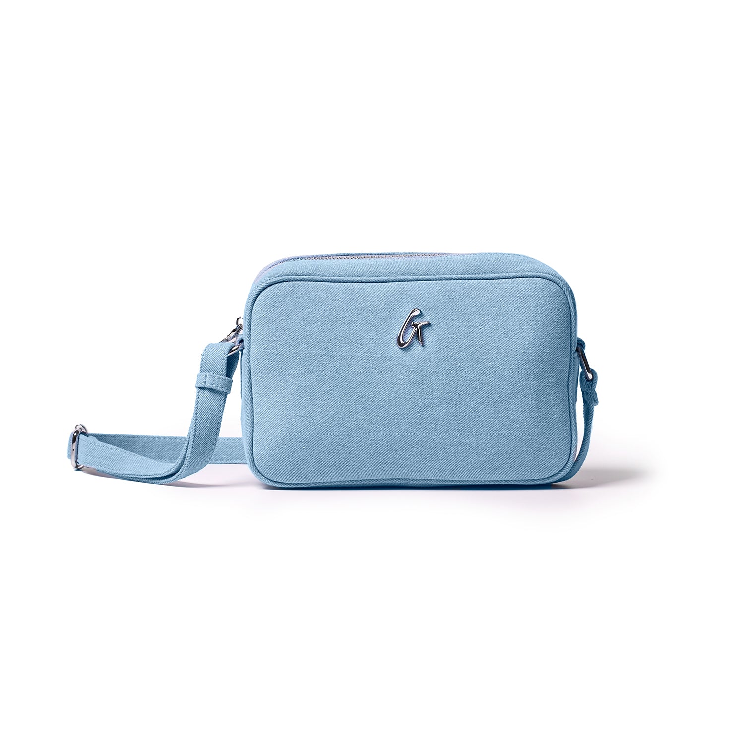 Light blue denim camera bag with a silver logo, adjustable strap, and zippered compartments on a white background.